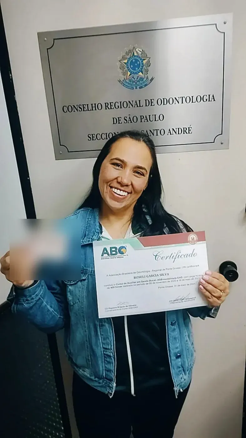 Aluna com o certificado do Curso ASB diante da placa do Conselho Regional de Odontologia de São Paulo