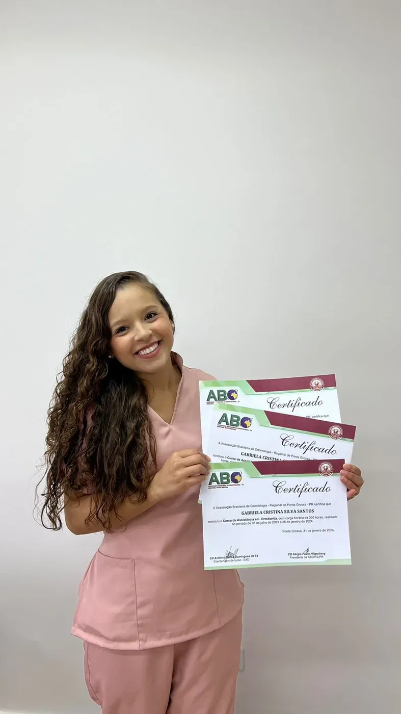 Aluna de pijama cirúrgico rosa segurando três certificados do Curso ASB