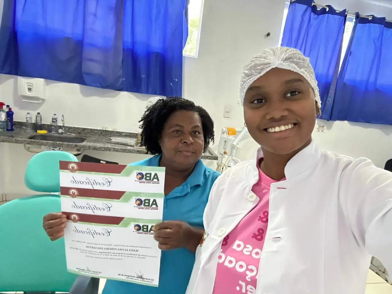 Duas alunas num consultório odontológico mostrando certificados do Curso ASB